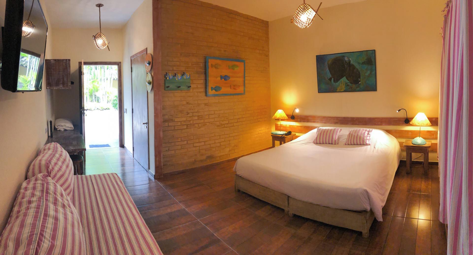 Habitación de hotel con cama, lámparas de noche, cabecera de madera, un ventanal grande y una puerta que da a un balcón.