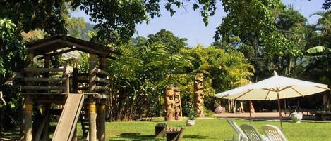 A park with a wooden play structure, a picnic area with a table and chairs, and lush greenery.