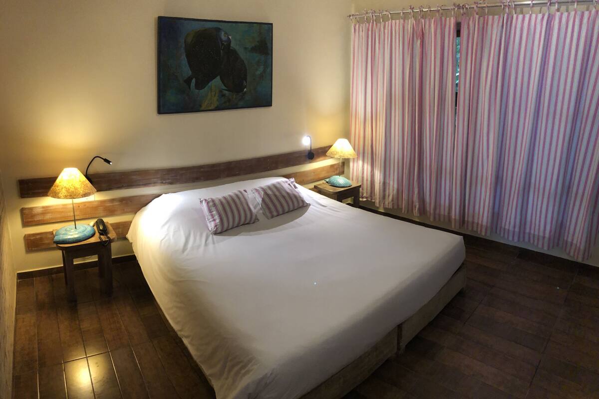 A hotel room with a large bed, two bedside tables with lamps, a striped curtain, and a painting on the wall.
