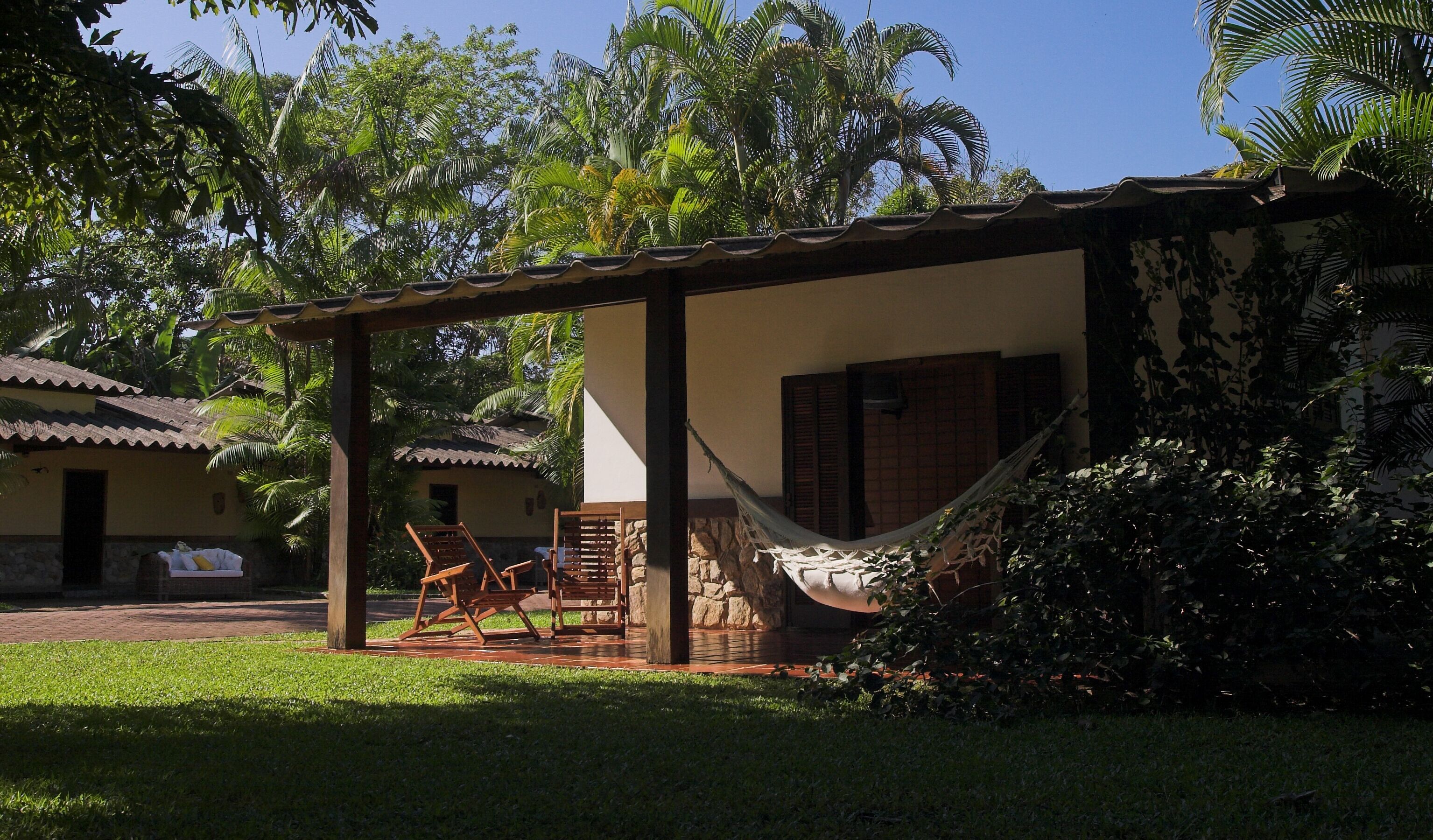 A covered outdoor seating area with a hammock, wooden chairs, and a small table.