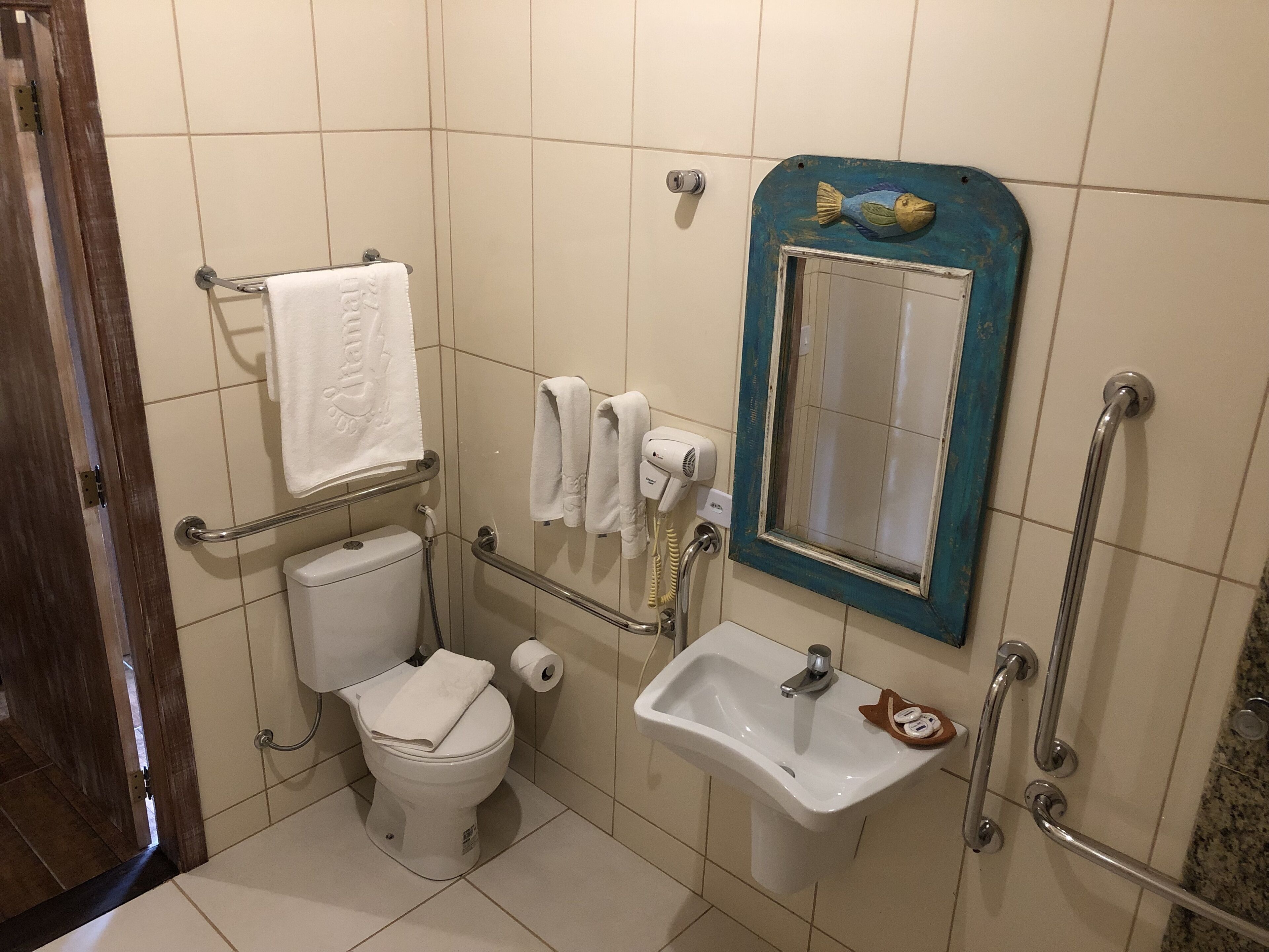 A bathroom with a toilet, sink, and hand dryer. There is a mirror with a blue frame and a towel rack.