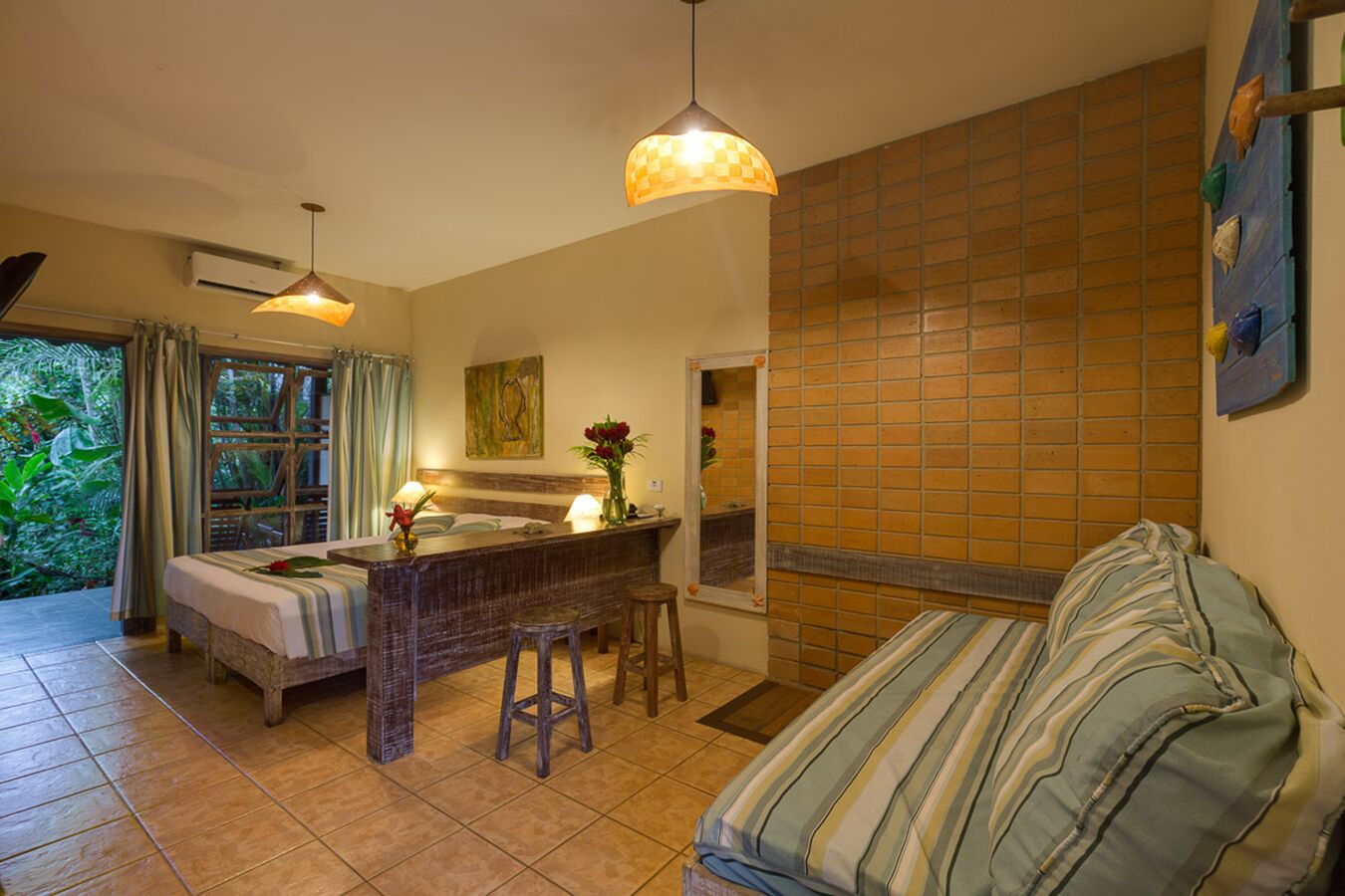 A room with a bed, a small bar area, a sofa, and a view of greenery outside.