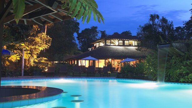 A swimming pool with lounge chairs and umbrellas, surrounded by lush greenery and a building with a tiled roof. - Itamambuca Eco Resort (Ubatuba)