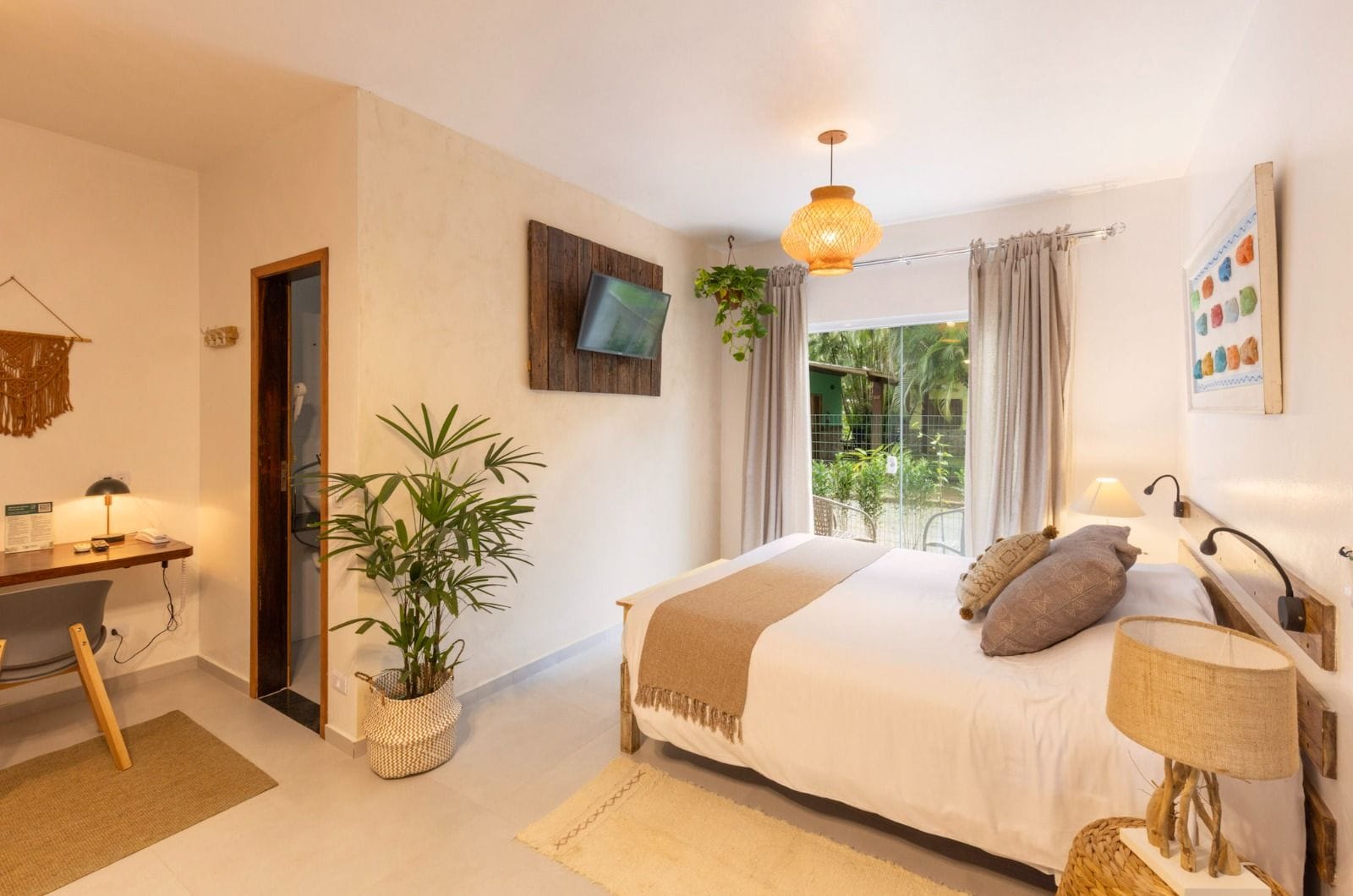 Quarto com cama, mesa de cabeceira, luminária, TV, janela com cortinas e uma planta.