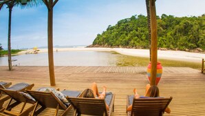 A wooden deck with lounge chairs facing a beach, surrounded by palm trees and a forested area. - Itamambuca Eco Resort (Ubatuba)