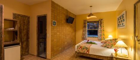 A bedroom with a bed, bedside lamps, a TV, a small table with a vase, and a door leading to another room.