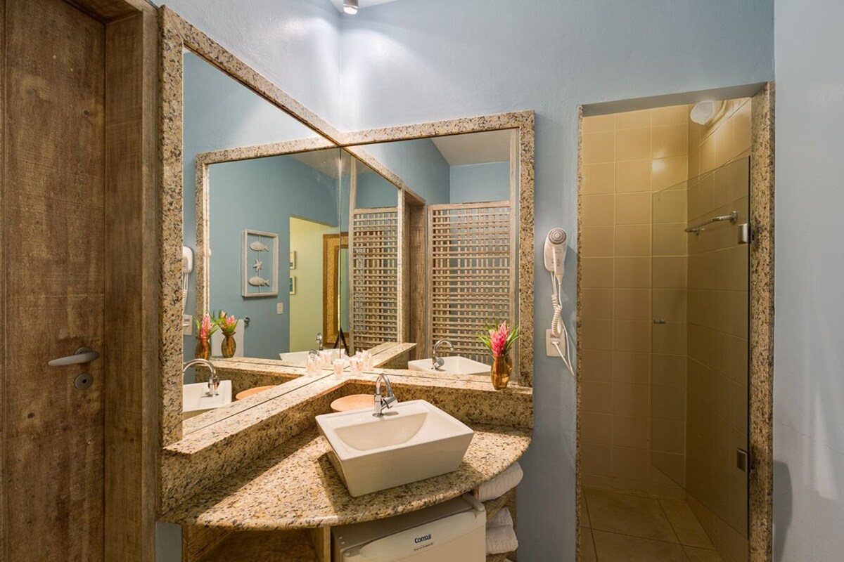 A bathroom with a large mirror, two sinks, a shower, and a door leading to another room.