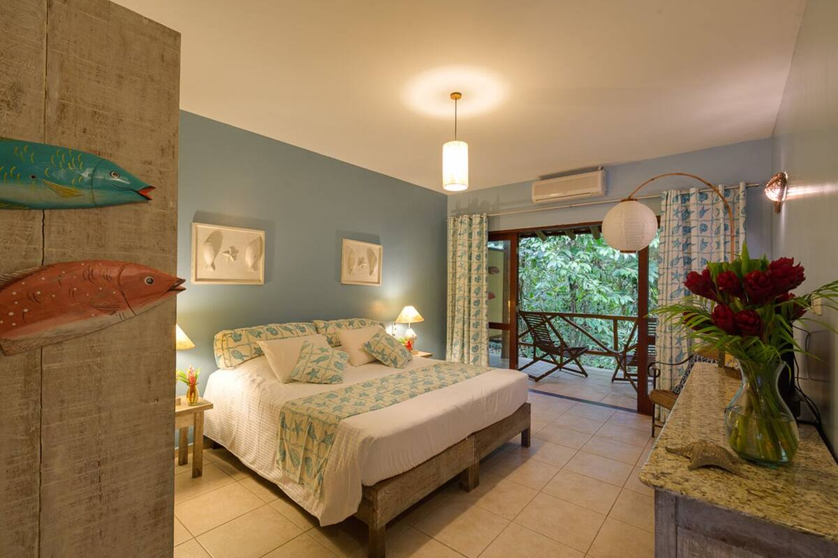 A bedroom with a bed, a nightstand, a lamp, and a view of the outdoors.