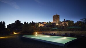 A swimming pool with lounge chairs and umbrellas, surrounded by a stone wall and trees, with a building and tower in the background. - B&B Borgo Petrognano - Residenza d'epoca (Barberino Tavarnelle)