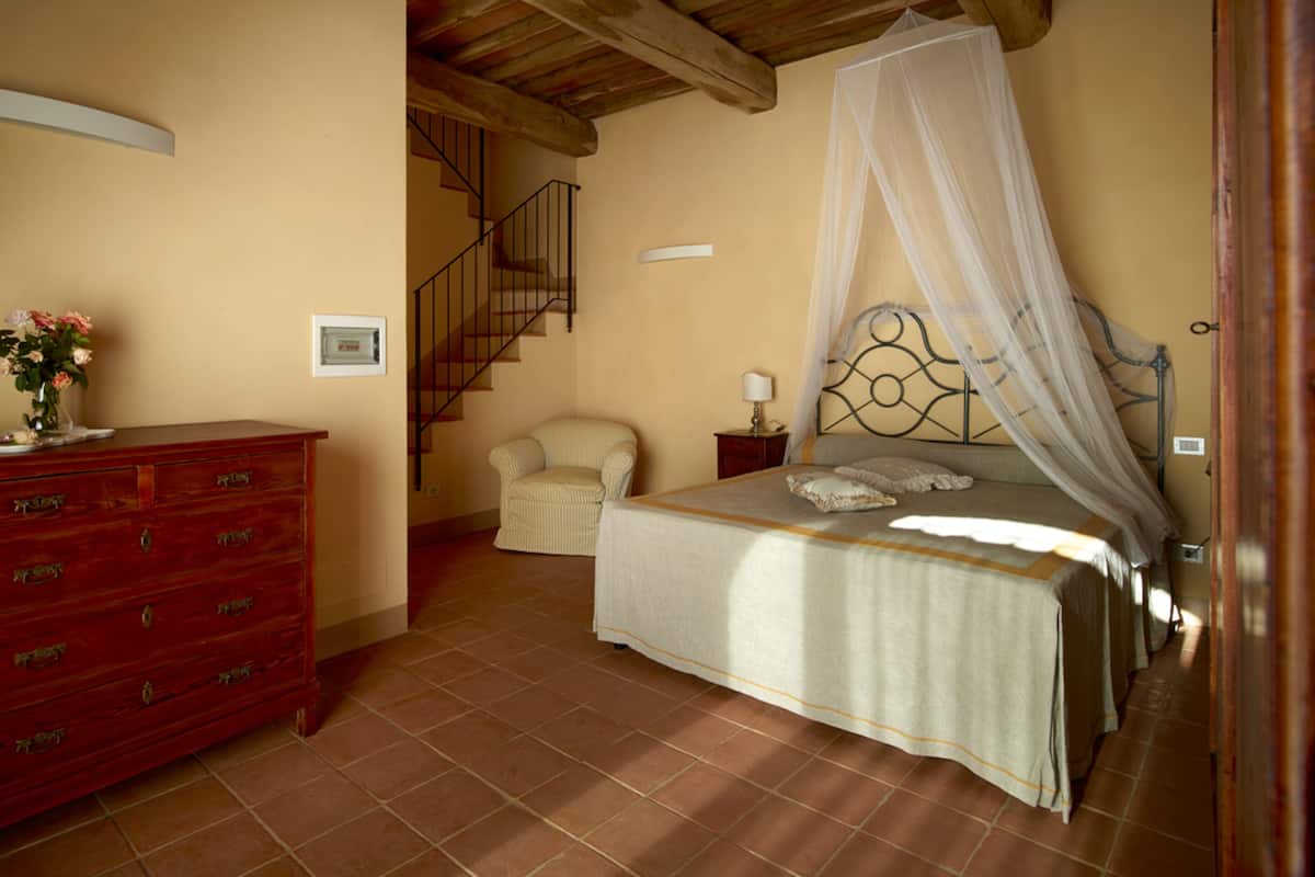 A bedroom with a bed, a nightstand, a chair, a dresser, and a staircase.
