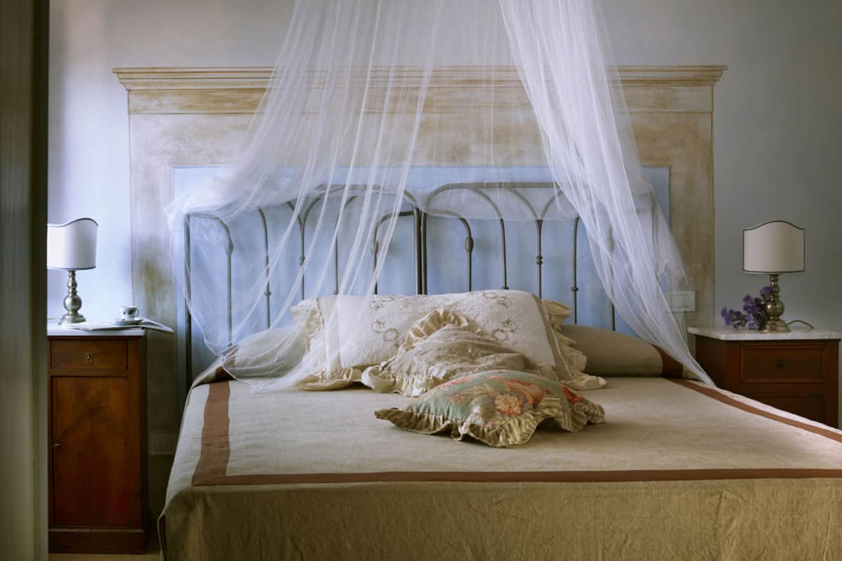 A bedroom with a canopy bed, two bedside tables with lamps, and a nightstand with a lamp.