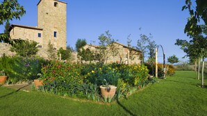 A stone building with a tower, surrounded by a well-maintained garden with various flowers and plants. - B&B Borgo Petrognano - Residenza d'epoca (Barberino Tavarnelle)