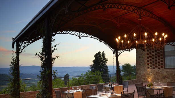 An outdoor patio with tables and chairs, a stone wall, and a view of the landscape. - B&B Borgo Petrognano - Residenza d'epoca (Barberino Tavarnelle)