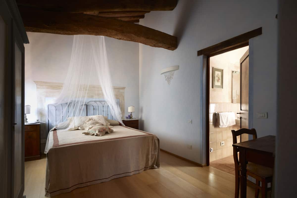 A bedroom with a bed, a bedside table, a chair, and a wooden ceiling.