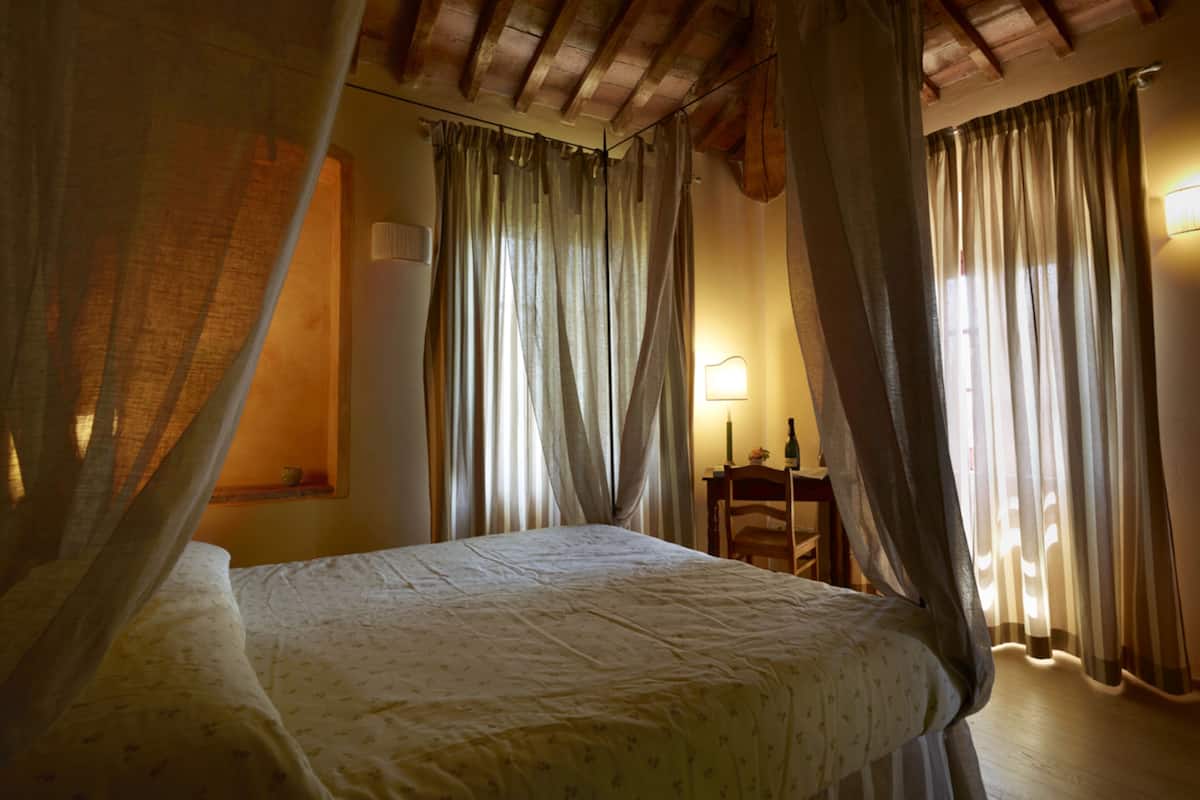 A bedroom with a bed, curtains, a nightstand, and a lamp.