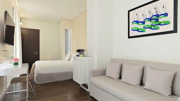 A modern hotel room with a bed, a sofa, a desk, and a painting on the wall.
