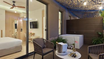 A modern hotel room with a balcony, a ceiling fan, a TV, and a dining area.