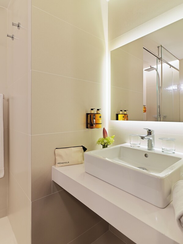 A modern bathroom with a large white sink, a glass shower enclosure, and a mirror above the sink.