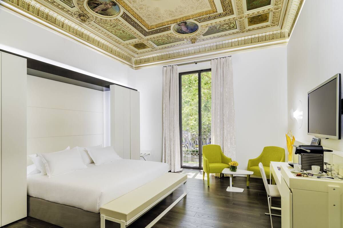 Ein modernes Hotelzimmer mit einem großen Bett, einem Schreibtisch mit Stuhl, einem Fernseher und einem Balkon mit Vorhängen.