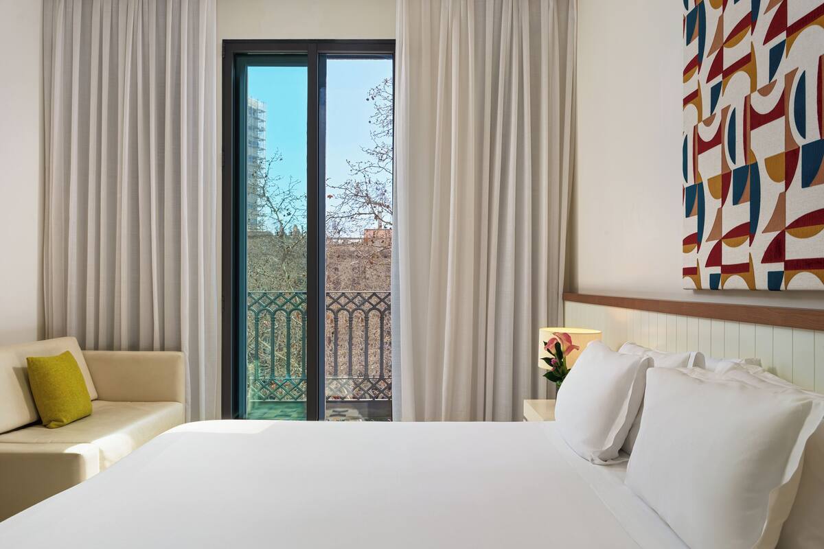 Ein Hotelzimmer mit Bett, Sofa, Nachttisch und einem Fenster mit Vorhängen.