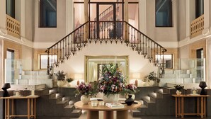 A grand staircase with a chandelier, a round wooden table, and a large mirror at the top.