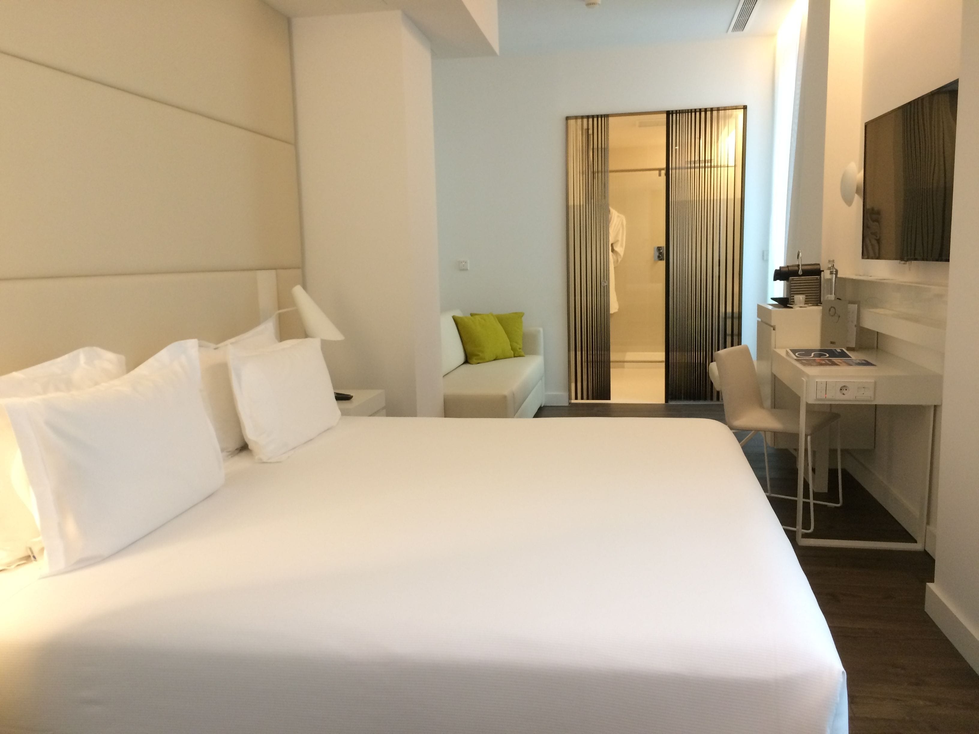 A modern hotel room with a large bed, a desk, and a walk-in closet.