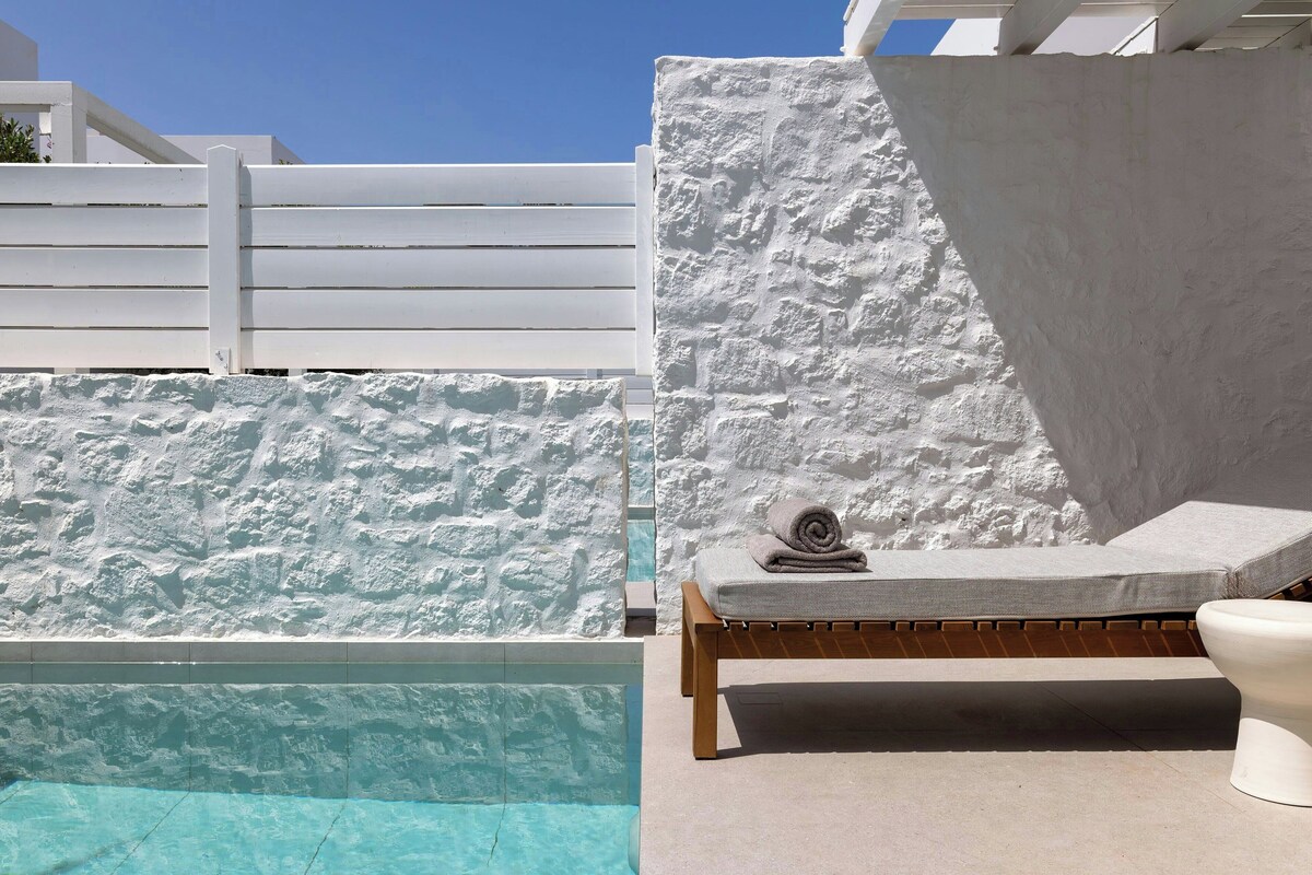 Un área de piscina con un muro blanco, una silla de descanso de madera y un inodoro blanco.