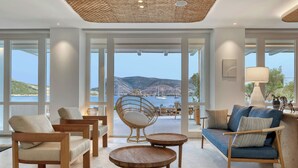 A spacious living area with large windows, a wicker chair, a blue sofa, and wooden furniture. - Patmos Aktis, a Luxury Collection Resort & Spa, Greece (Patmos)