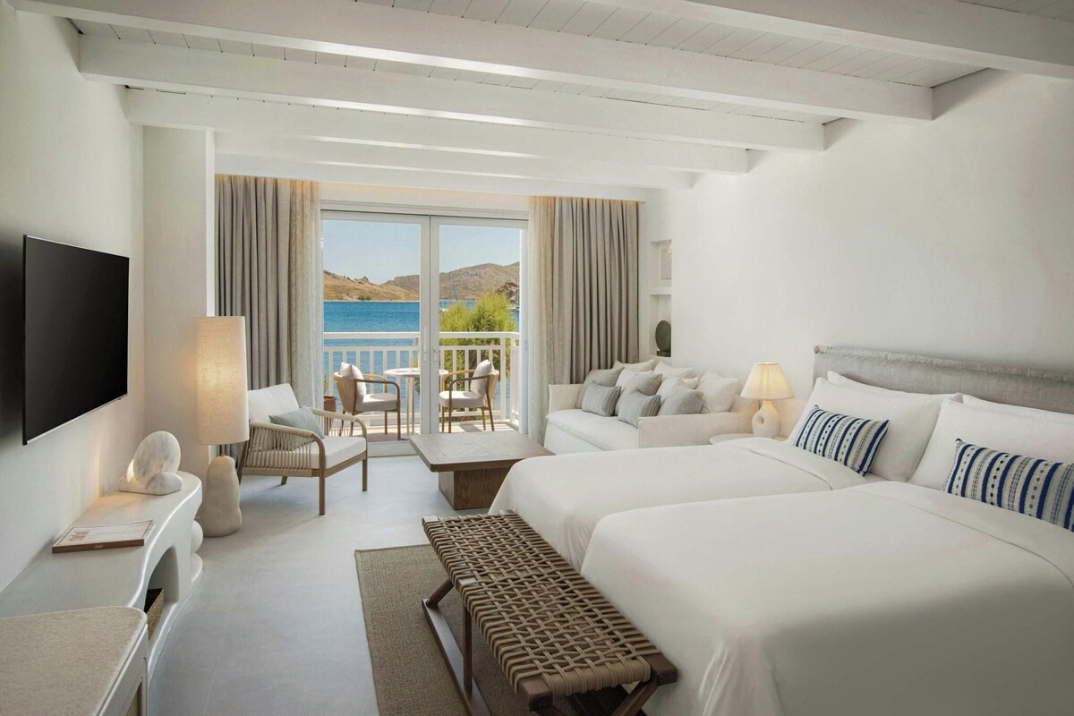 Habitación de hotel con cama, escritorio, silla, sofá, televisor y vista al mar.