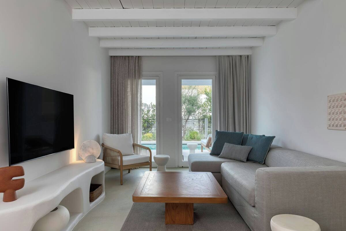 Ein modernes Wohnzimmer mit Flachbildfernseher, Couchtisch aus Holz, grauem Sofa und weißem Sessel.
