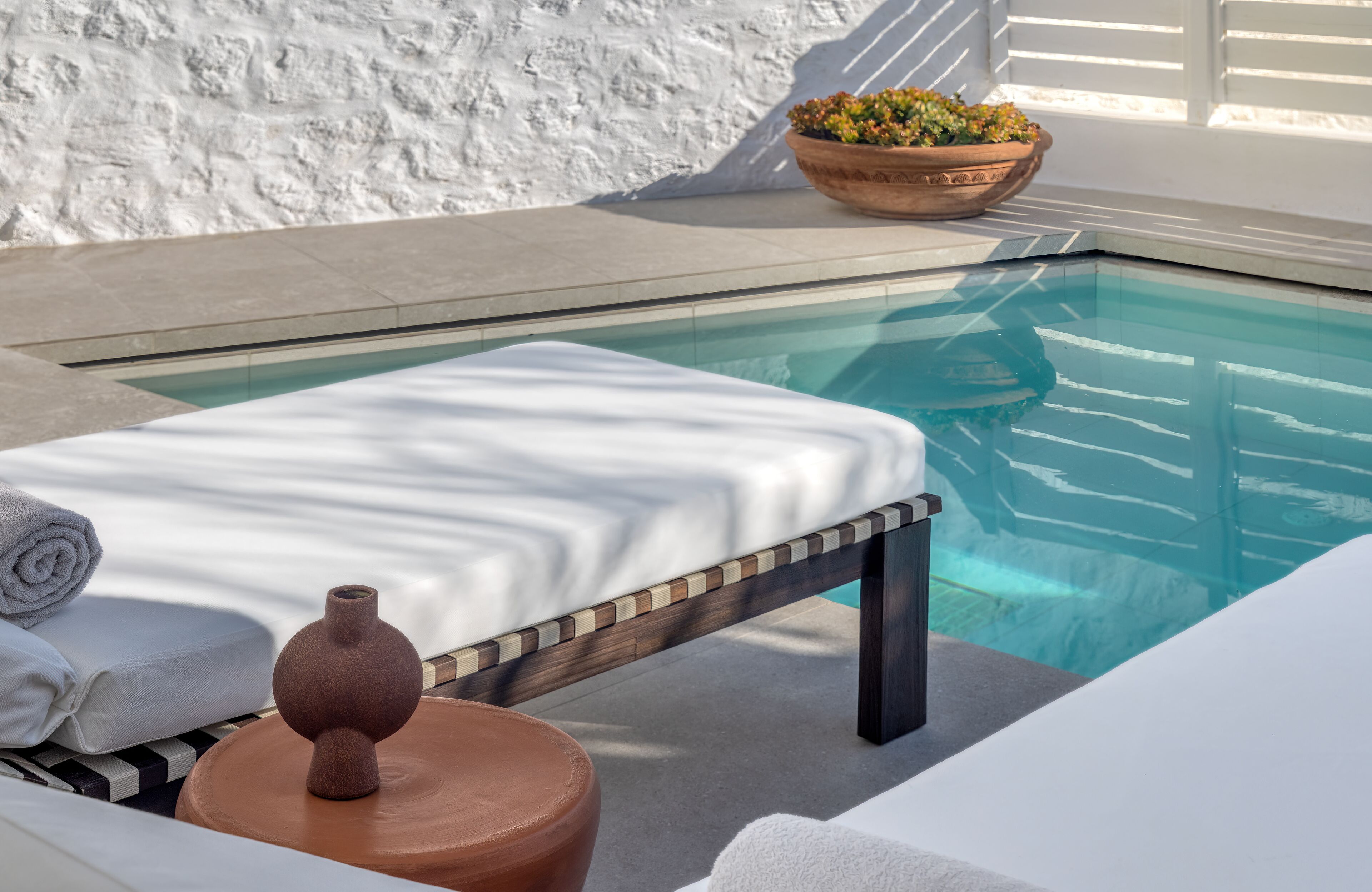 A poolside area with a sun lounger, a small table with a vase, and a potted plant.