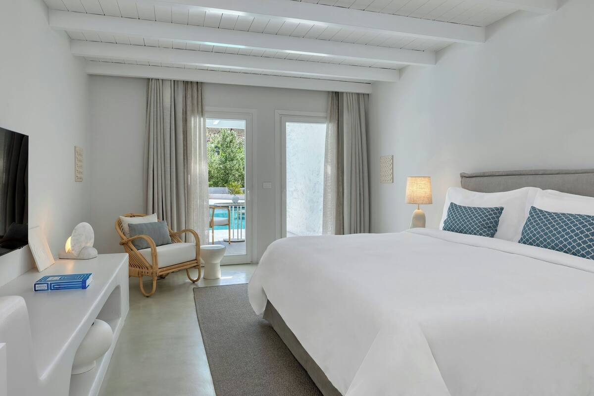 Ein modernes Hotelzimmer mit einem großen Bett, einer Sitzecke mit einem Sessel, einem kleinen Tisch und einem Fernseher.