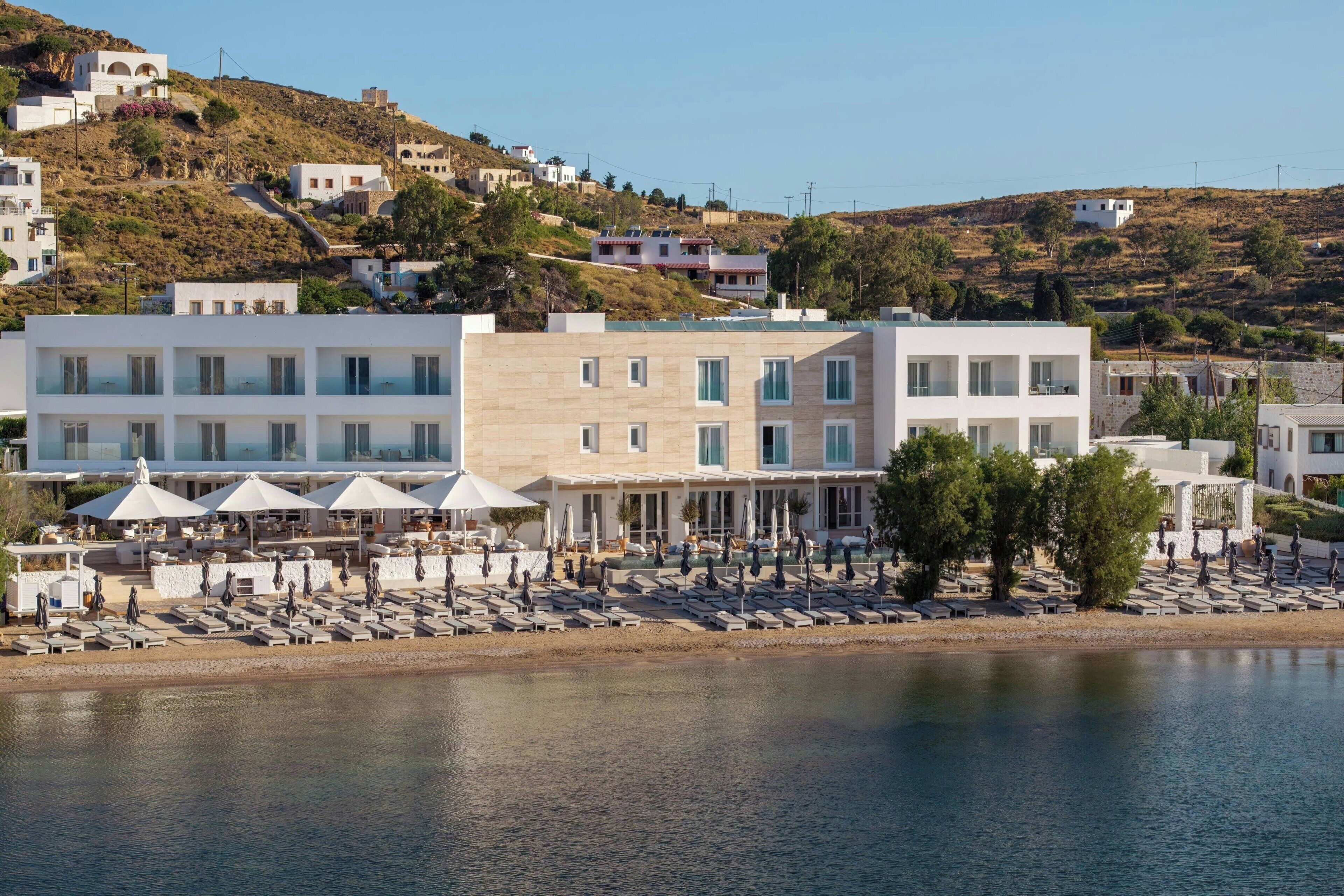 A coastal hotel with multiple floors, outdoor seating, and a view of the sea.