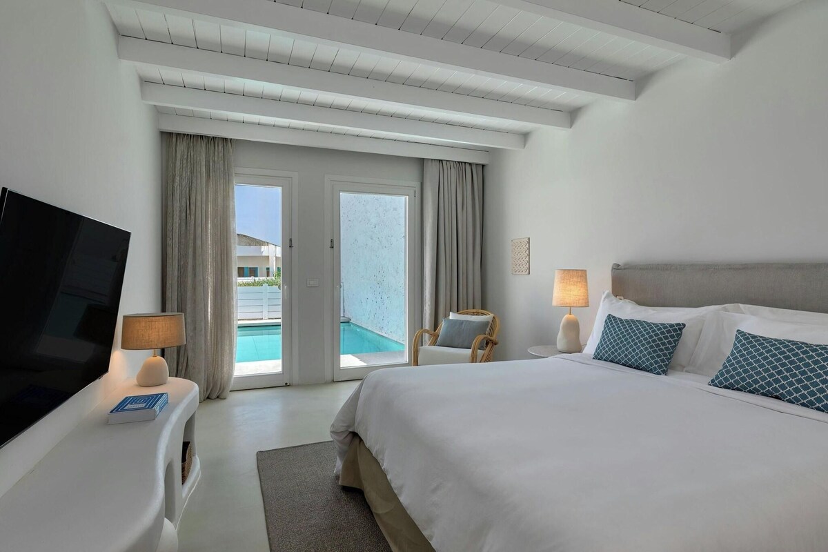 Habitación de hotel con cama, televisión, lámpara y vista a una piscina.