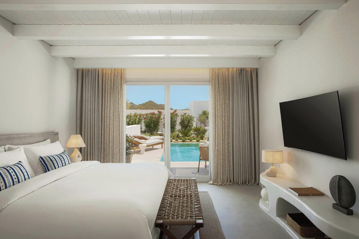 Habitación de hotel con cama, televisión, escritorio y vistas a una piscina y jardín.