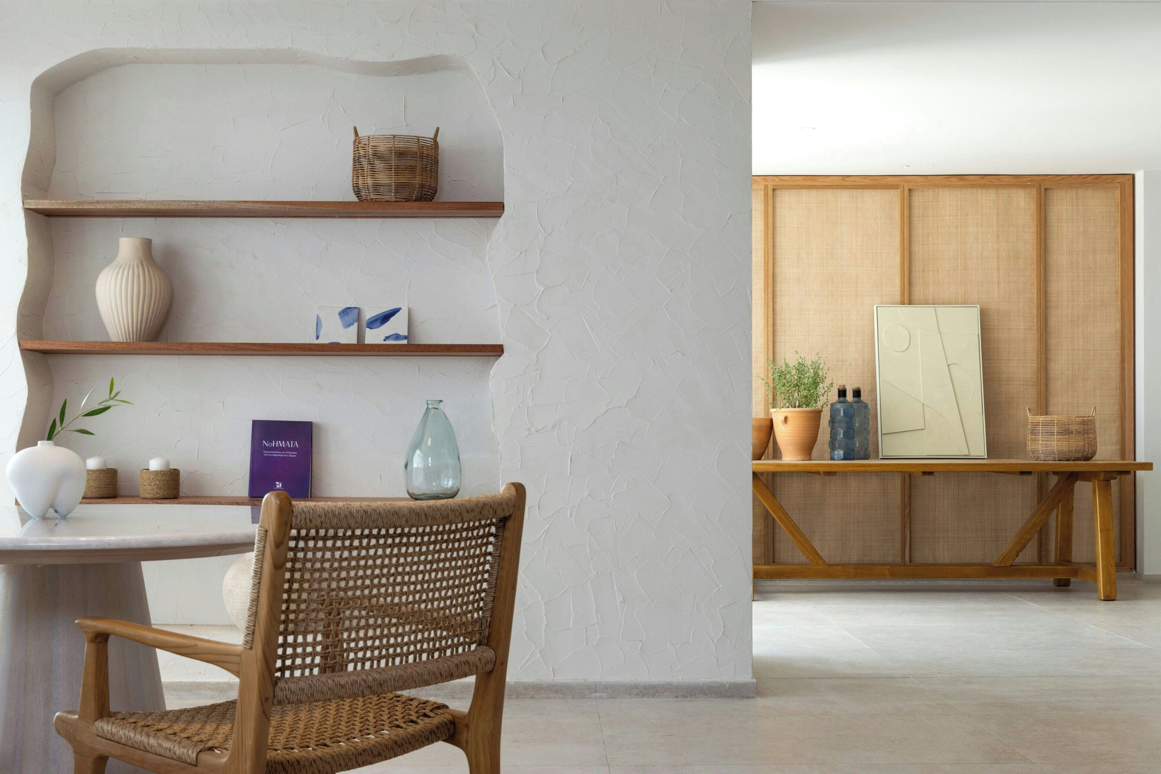 A room with a wooden chair, a white vase, a wicker basket, and a shelf with decorative items.