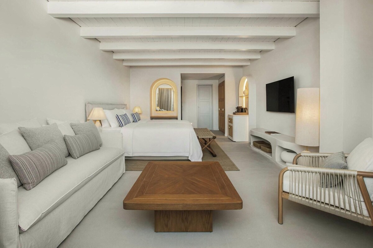 Una habitación de hotel moderna con cama, sofá, sillón y televisión.