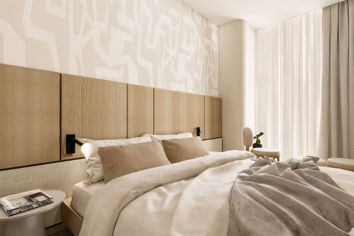 Une chambre d’hôtel moderne avec un grand lit, une table de chevet avec un magazine, une petite table d’appoint et une chaise.