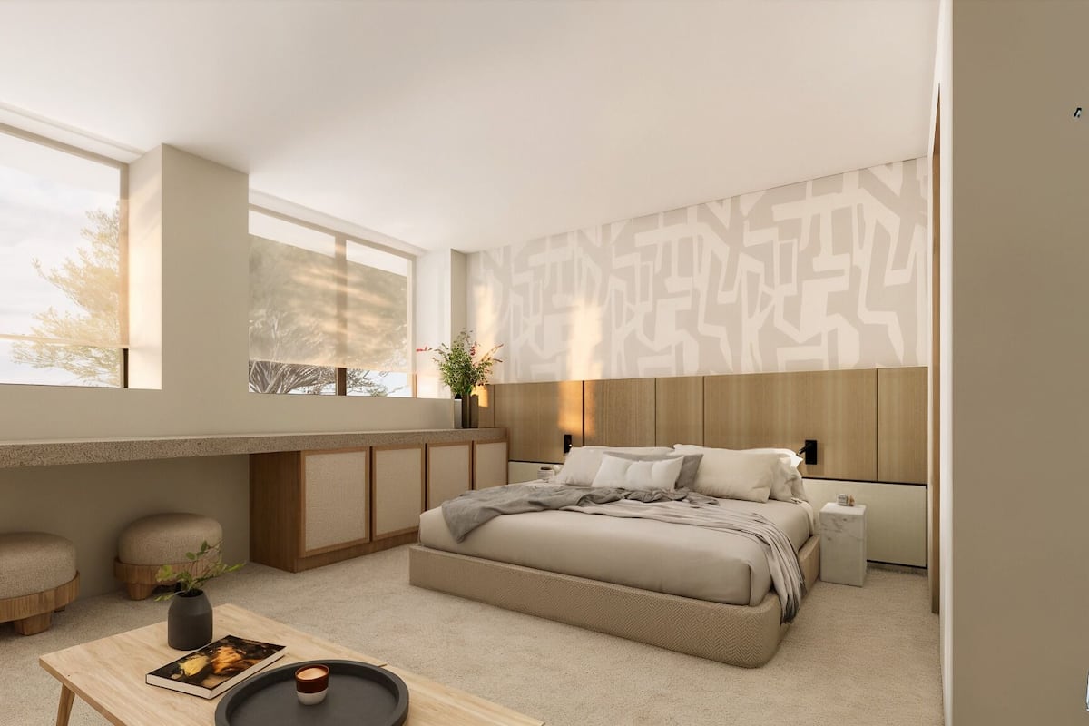 Une chambre moderne avec un grand lit, un coin salon avec des poufs, une petite table sur laquelle se trouvent un livre et une bougie, et une vue sur les arbres à travers de grandes fenêtres.