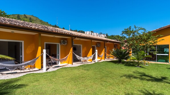A yellow building with multiple doors and windows, a grassy lawn, and a hammock in the foreground.