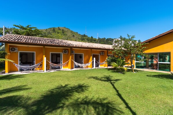 A yellow building with a tiled roof and multiple windows, surrounded by a well-maintained lawn and a hammock. - Pousada Villa Piemonte (Ubatuba)