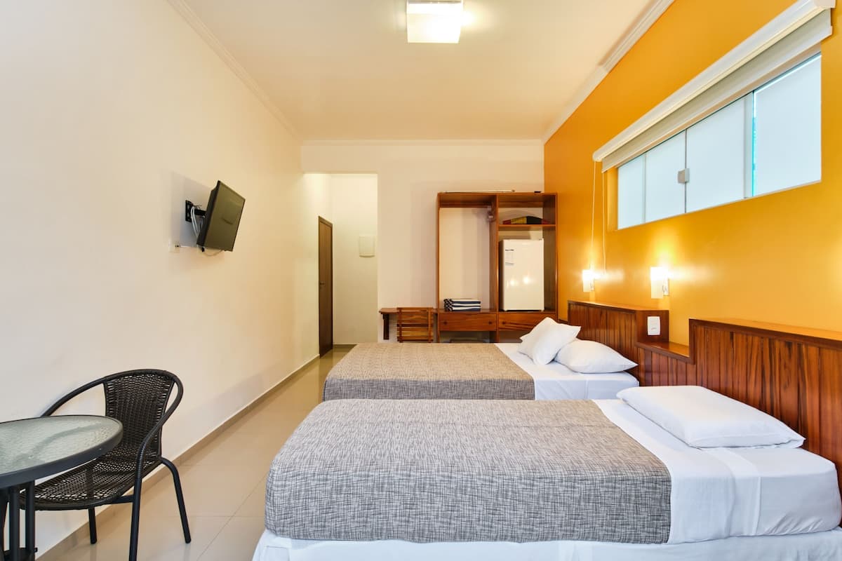 A hotel room with two beds, a desk, a chair, a wardrobe, and a television mounted on the wall.