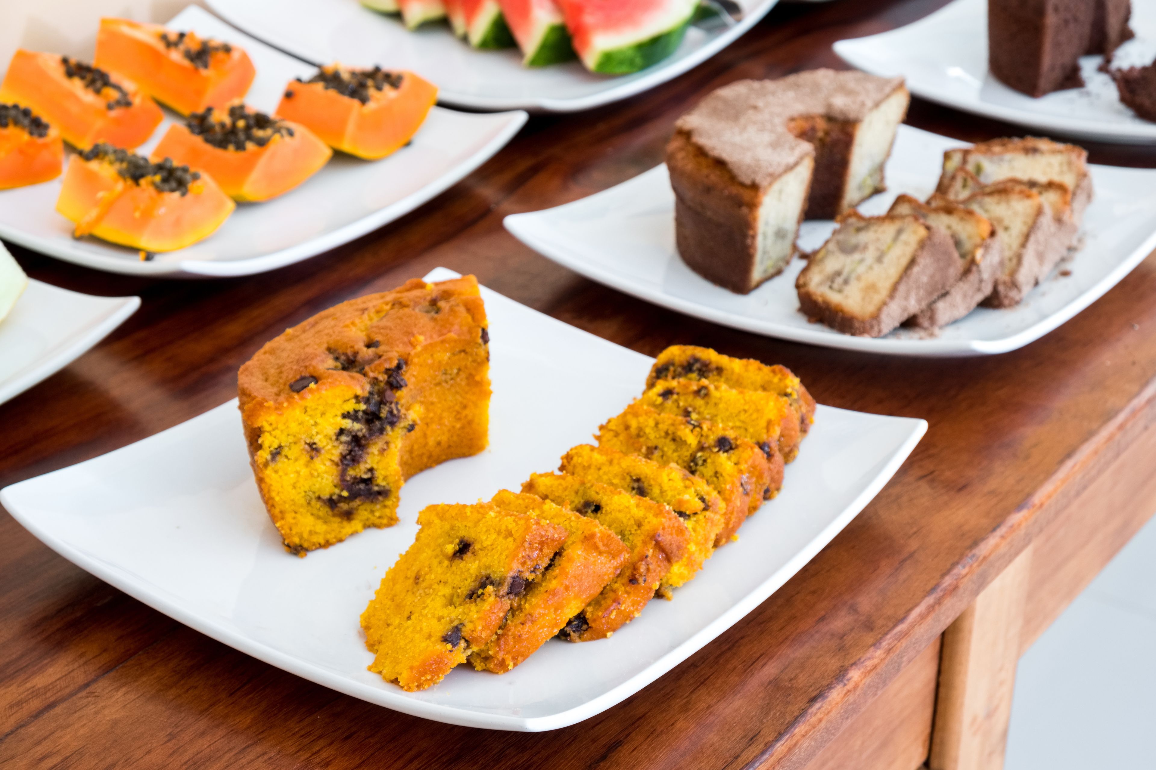 A variety of desserts on white plates, including slices of cake and fruit.