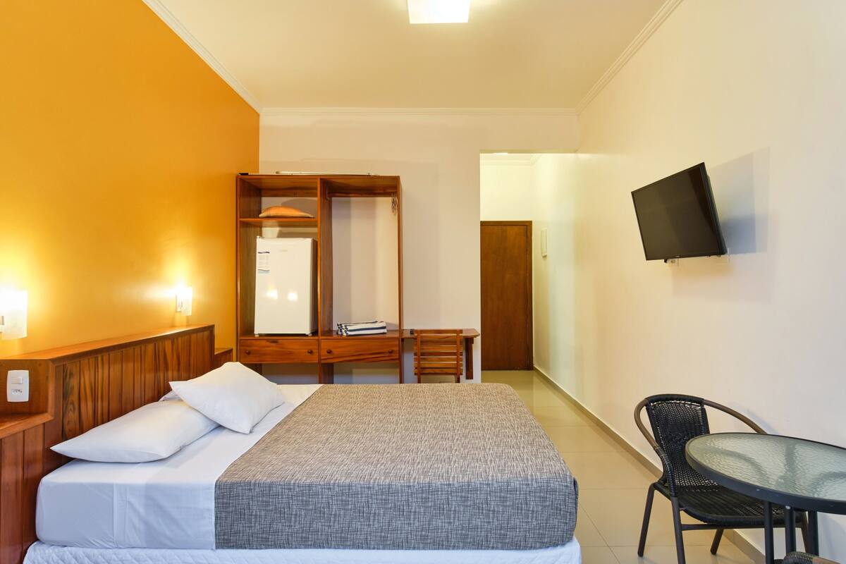 A hotel room with a bed, a desk, a chair, a TV, and a wardrobe.
