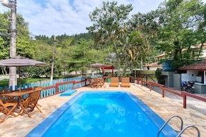 A swimming pool with lounge chairs and umbrellas, surrounded by a wooden fence and greenery. - Pousada Villa Piemonte (Ubatuba)