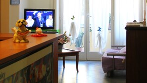Un soggiorno con televisione, un divano, un tavolino da caffè e una porta vetrata scorrevole che dà su un balcone.