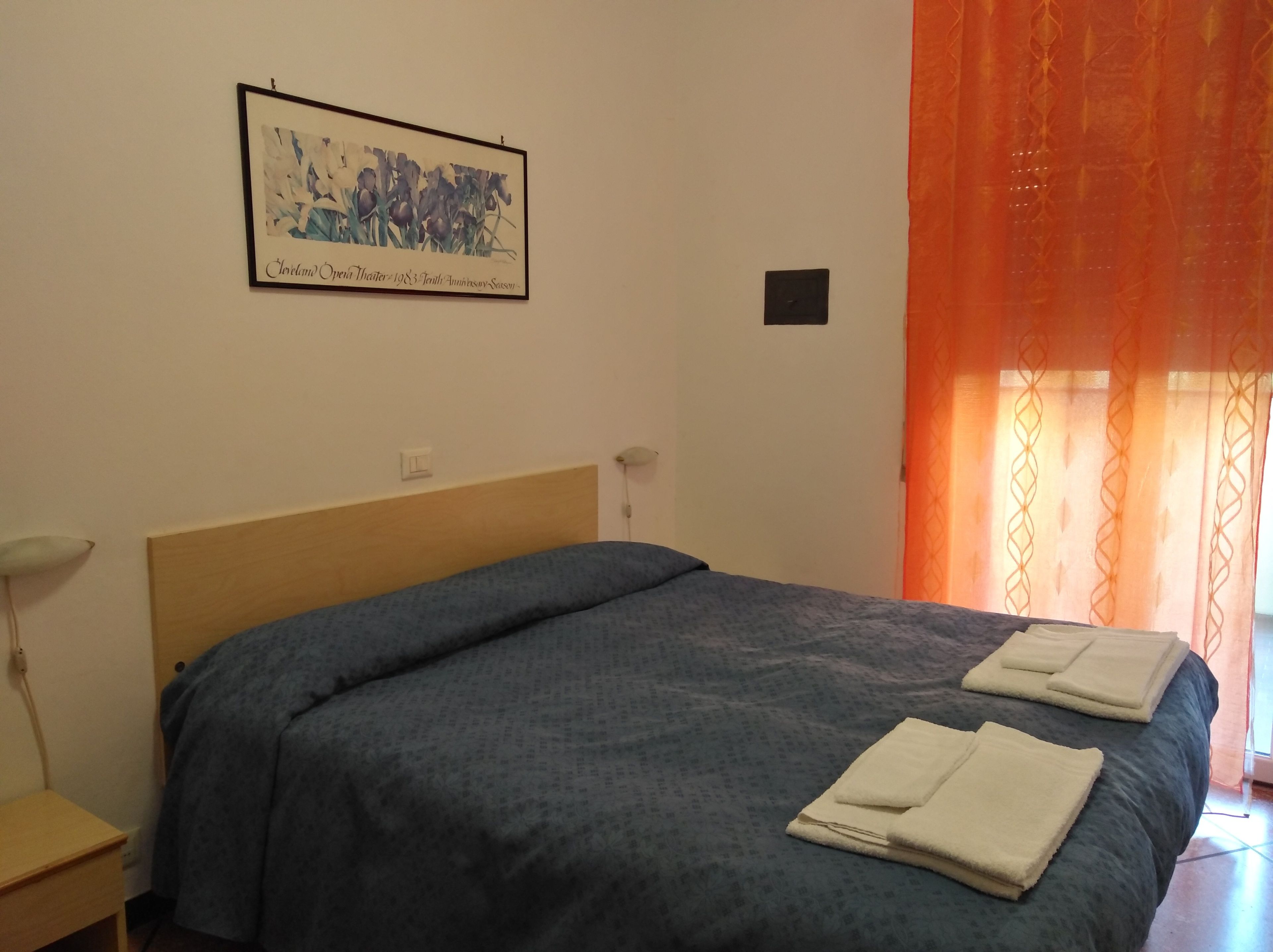A bedroom with a bed, a nightstand, a framed picture on the wall, and orange curtains.