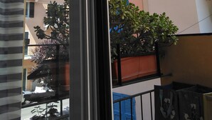 Vista attraverso una finestra di un edificio con balconi, piante in vaso e cielo sereno.