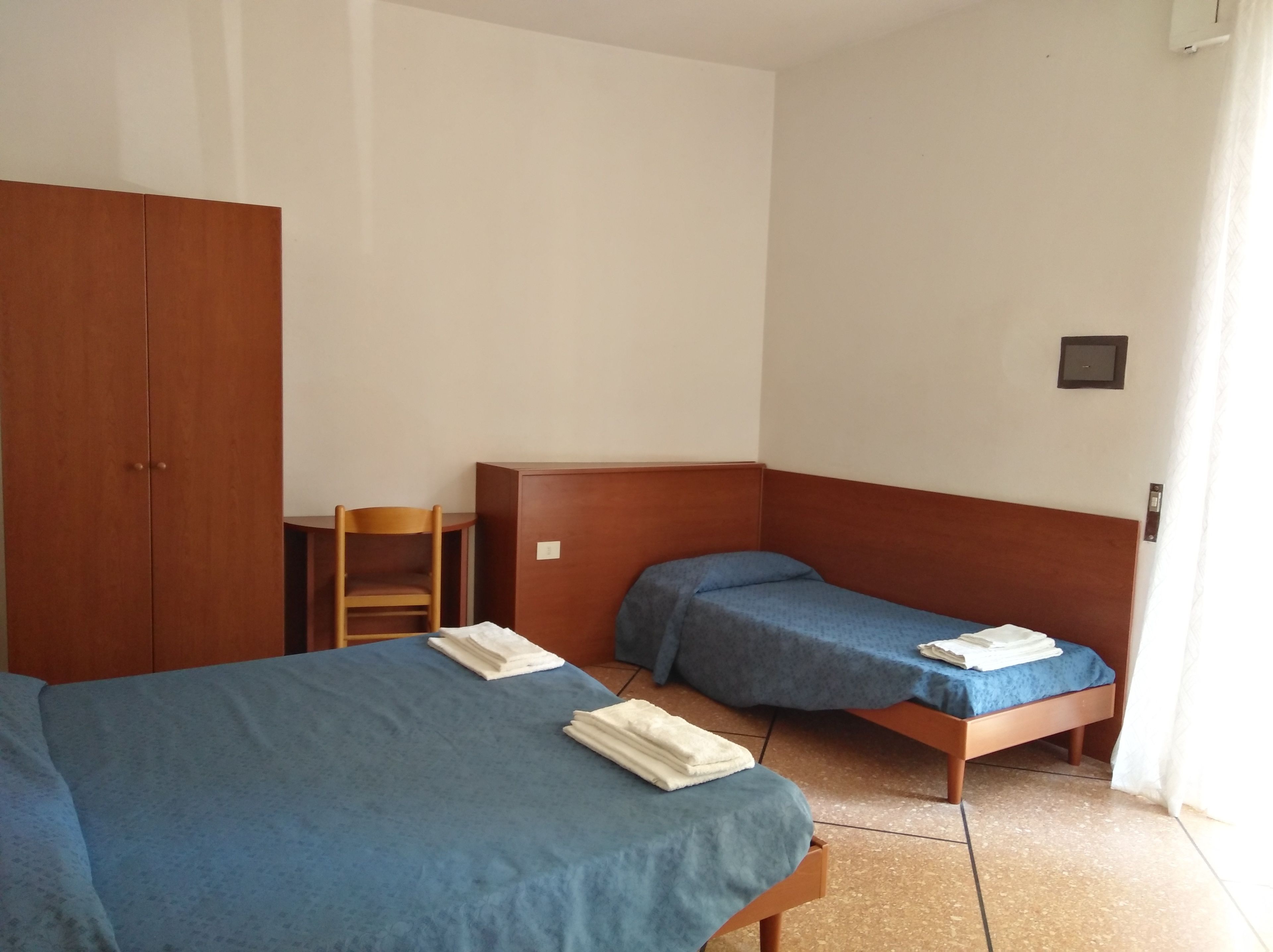 Een kamer met twee bedden, een houten kast, een klein tafeltje en een stoel.