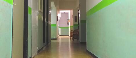 A long, narrow hallway with tiled flooring and green and white walls. There are doors on both sides, and a few framed pictures on the right wall.